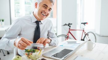 Happy businessman opening his salad pack and having a lunch break at office desk enjoying healthy eating